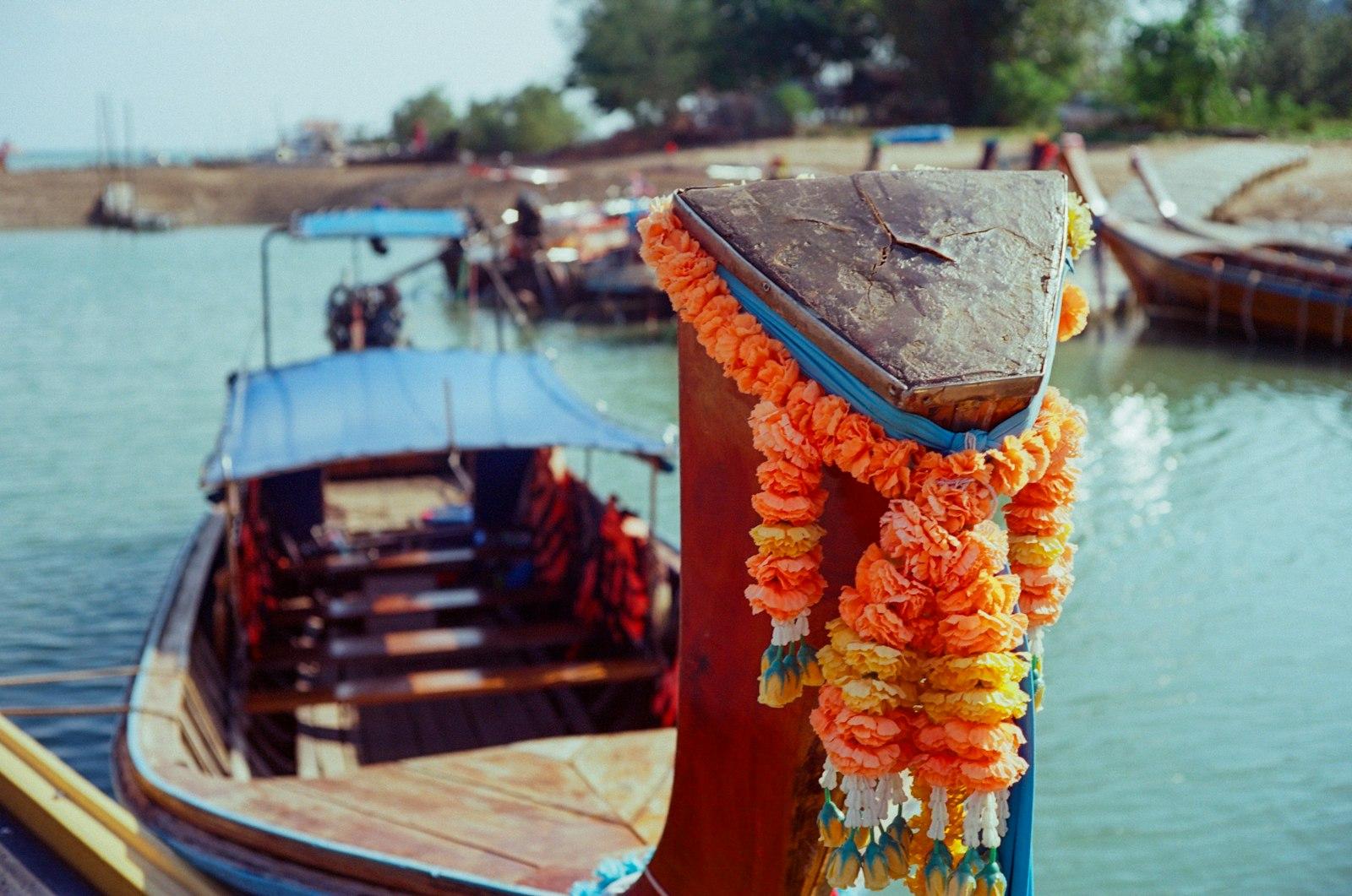 Close-up of an orange and yellow flower garland tied to the bow post of a wooden longtail boat