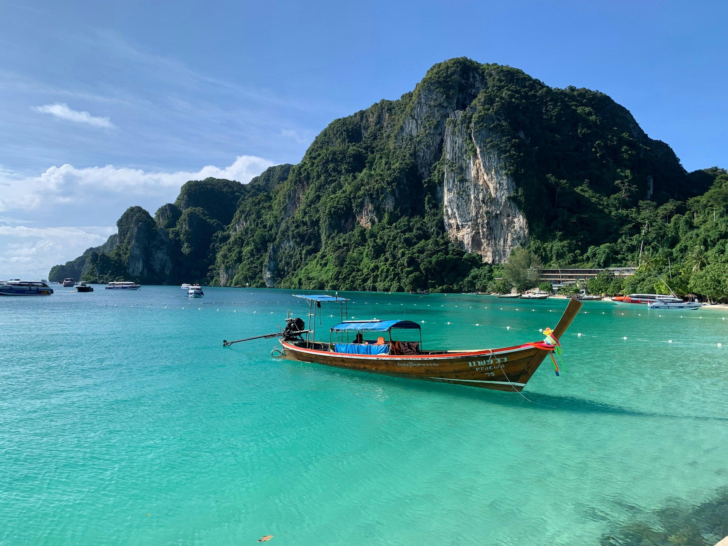 A traditional Thai longtail boat in clear turquoise water beneath limestone karst cliffs
