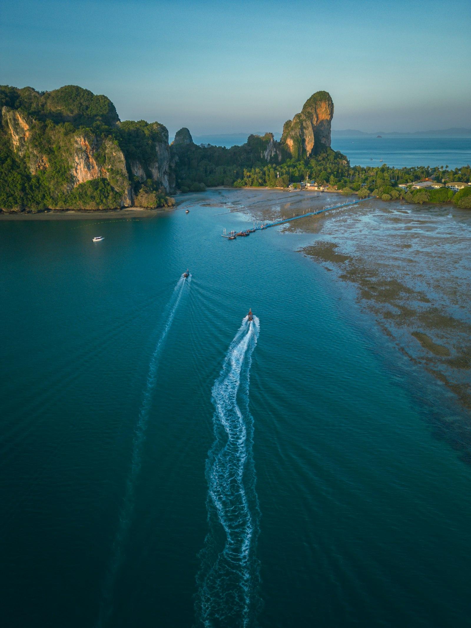 Aerial view of two speedboats crossing turquoise water near limestone cliffs, long white wakes trailing behind