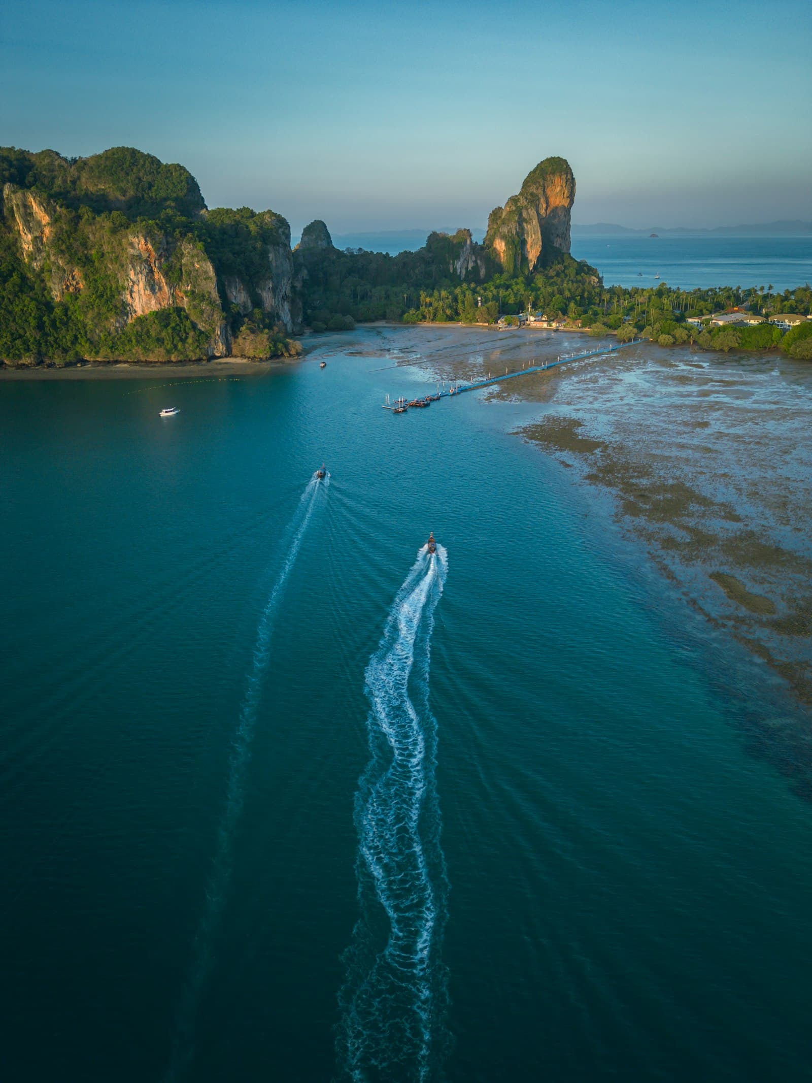 Aerial view of two speedboats crossing turquoise water near limestone cliffs, long white wakes trailing behind